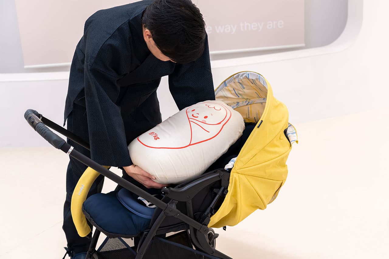 赤ちゃんの体重を想定したおもりのぬいぐるみをベビーカーに乗せる作務衣の男性