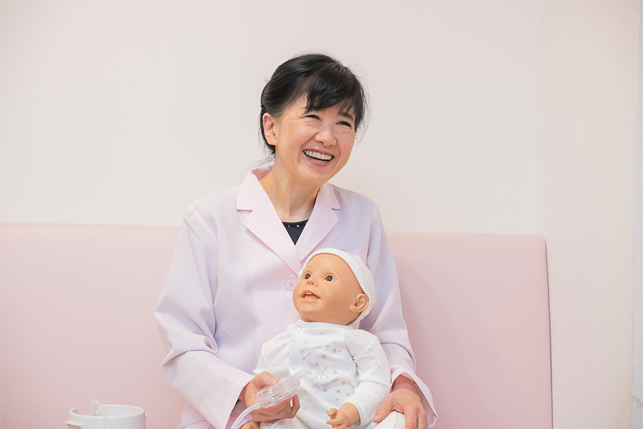 鼻吸い器を片手に持って、赤ちゃん人形を抱っこした笑顔の木村先生です。