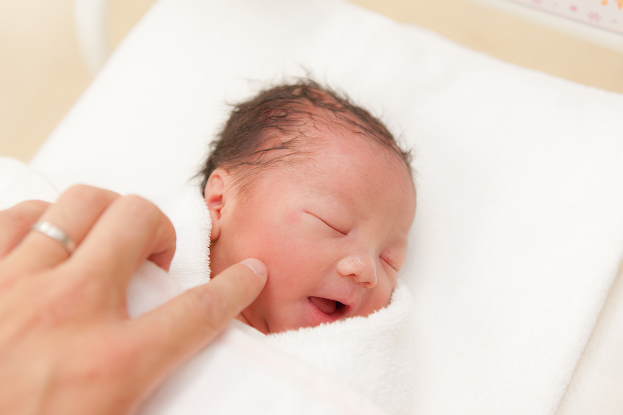 新生児らしい赤ちゃんのほっぺを指で触っている