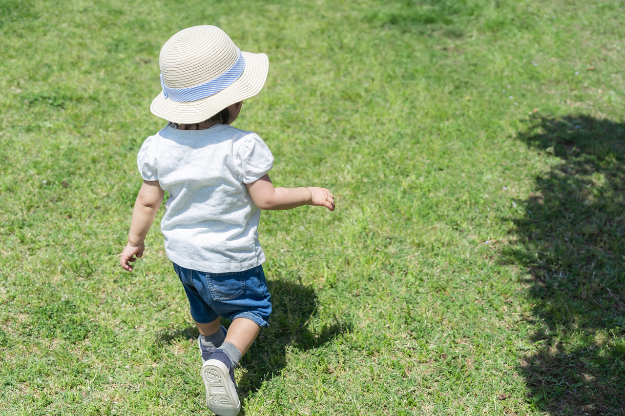 帽子をかぶって芝生の上を歩いている赤ちゃん