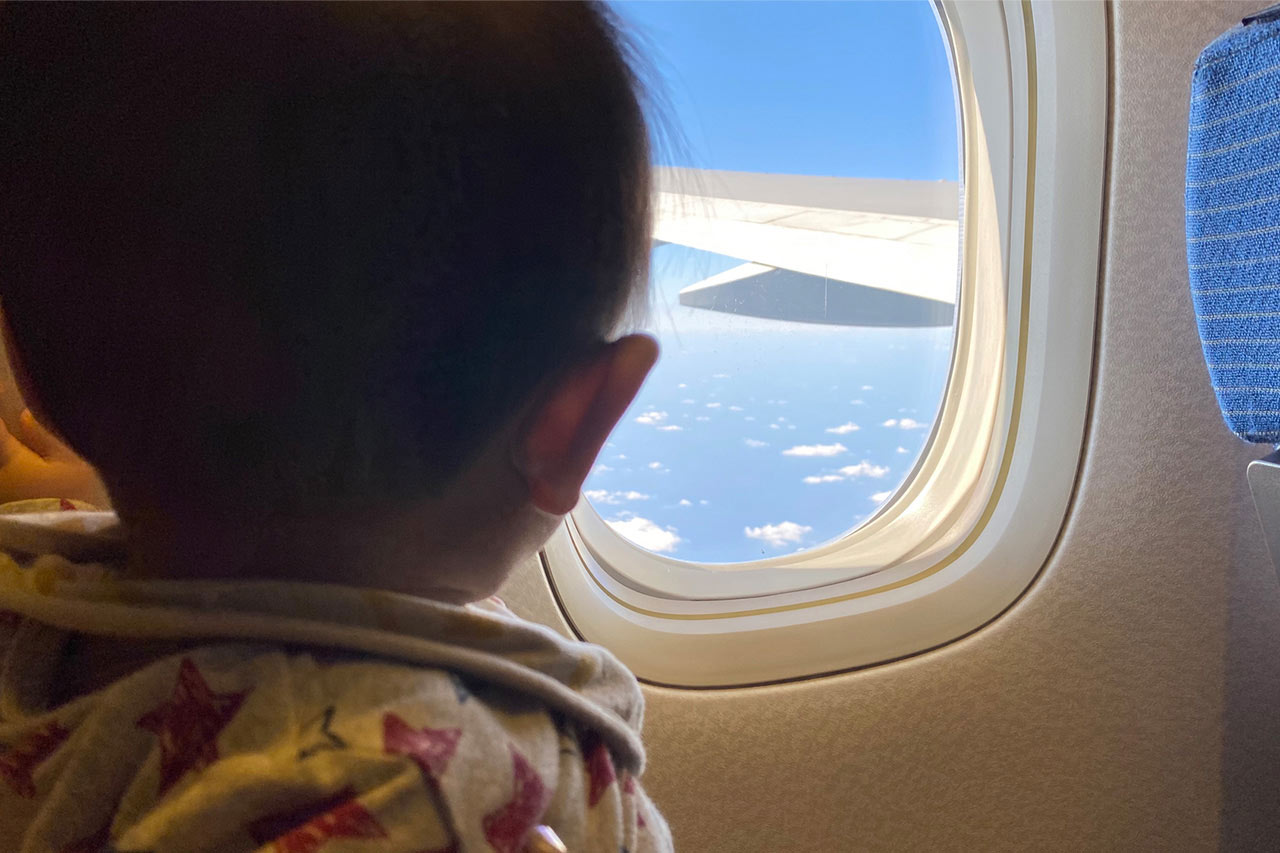 赤ちゃんが飛行機の窓から外を見ている画像